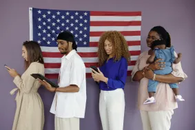 Four people stand in front of a U.S. flag, three using electronic devices—perhaps consulting a mandamus lawyer online—and one holding a baby.