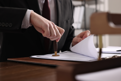 A mandamus lawyer in a suit stamps a document on a desk, suggesting official approval or legal authorization.