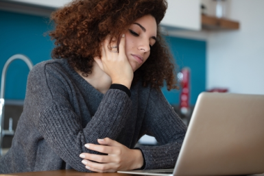 A person with curly hair sits at a table, resting their head on their hand and looking at a laptop screen with a tired expression—perhaps researching the next steps with a mandamus lawyer.