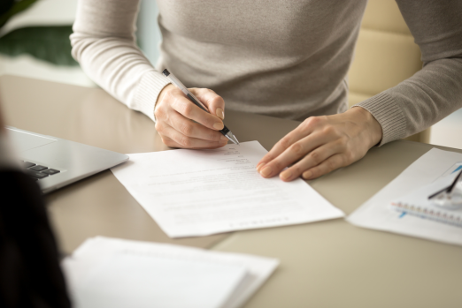 A mandamus lawyer sits at a desk, signing a document with a pen beside a laptop and a notebook.