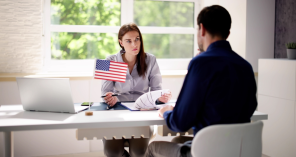 A woman holding a small American flag sits at a desk with documents, consulting with a mandamus lawyer across from her in an office setting.