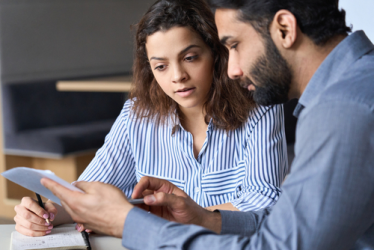 Two people sitting at a table—a mandamus lawyer holding a notepad and pen, the other showing a document—engaged in a focused discussion.