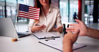 Two people sit at a desk with documents, a laptop, and a small American flag, consulting with a mandamus lawyer in a modern office setting.