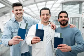 Three men standing together in an airport terminal, each holding a passport and boarding pass, smiling at the camera—perhaps preparing for their journey with the help of a mandamus lawyer.